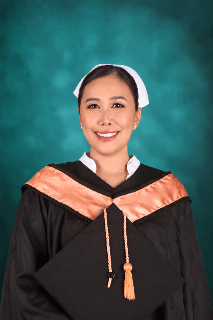 A smiling graduate wearing a black academic gown with orange accents and a mortarboard cap, set against a turquoise background.